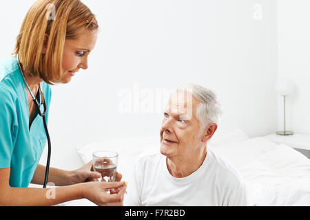 Il vecchio uomo getting medicine e acqua da infermiere in casa di cura Foto Stock