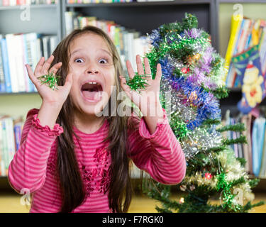 Ragazza giovane decorare albero di Natale rendendo divertente volto Foto Stock