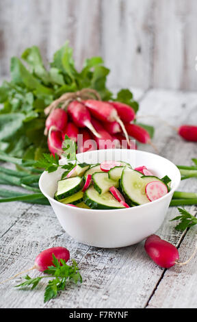 Insalata fresca di cetrioli e ravanelli in una ciotola bianco sul vecchio sfondo di legno Foto Stock