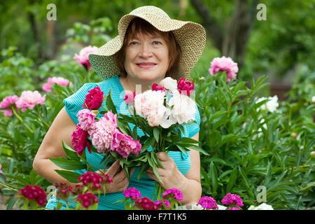 Felice donna matura in peonia pianta in giardino Foto Stock