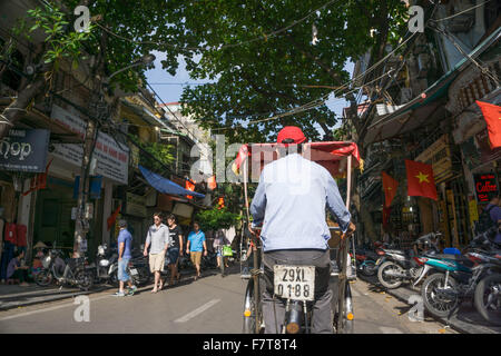 Hanoi, Vietnam: un driver cyclo passa di una tipica scena di strada di Hanoi la vibrante quartiere vecchio. Foto Stock