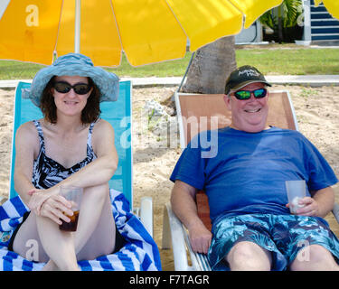 A 50 anni coppia caucasica in rilassanti sedie a sdraio sotto gli ombrelloni sulla spiaggia di St. Croix, U.S. Isole Vergini. USVI, U.S.V.I. Foto Stock