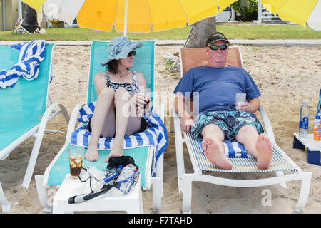 A 50 anni coppia caucasica in rilassanti sedie a sdraio sotto gli ombrelloni sulla spiaggia di St. Croix, U.S. Isole Vergini. USVI, U.S.V.I. Foto Stock