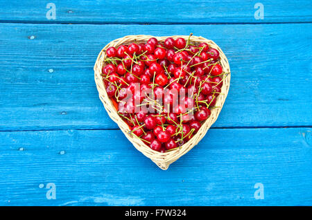 A forma di cuore cesto in vimini pieno di ciliegie blu sul vecchio tavolo da giardino sullo sfondo di legno Foto Stock