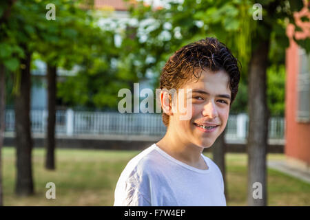 Adolescente con acne pelle sorridere mentre mostra le bretelle con alberi in background Foto Stock