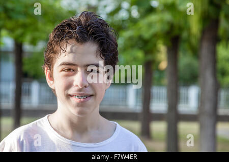 Adolescente con acne pelle sorridere mentre mostra le bretelle con alberi in background Foto Stock