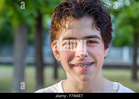 Adolescente con acne pelle sorridere mentre mostra le bretelle con alberi in background Foto Stock