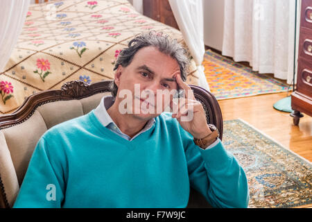 Uomo di mezza età seduto in camera da letto tiene il suo tempio con un dito di una mano mentre medita Foto Stock