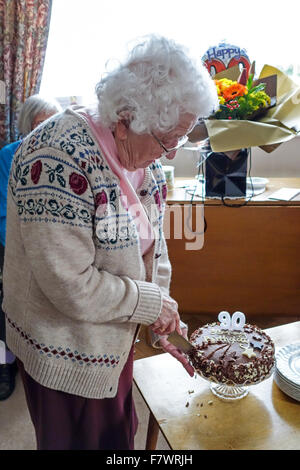 Una donna anziana che celebra il suo novantesimo compleanno e il taglio la sua torta di compleanno Foto Stock