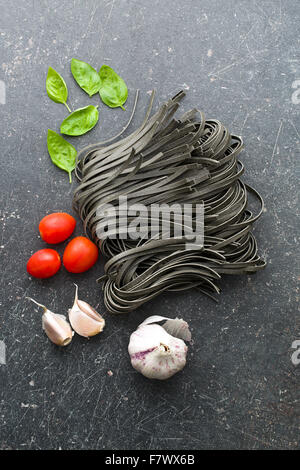 Tagliatelle, aglio, pomodori e basilico foglie sul vecchio tavolo da cucina Foto Stock