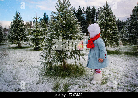 Ragazza appesa decorazione di Natale su un albero al di fuori nella neve Foto Stock