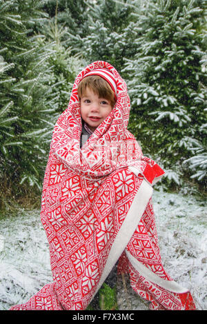 Ragazzo che sta al di fuori nella neve, avvolto in una coperta Foto Stock