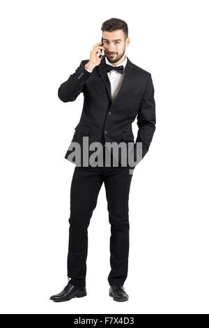Sorridente uomo bello in formale parlare di usura sullo smartphone guardando la fotocamera. Corpo pieno lunghezza ritratto isolato su bianco Foto Stock