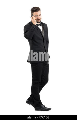 Vista laterale del giovane imprenditore della tuta camminare e parlare al telefono cellulare testa di tornitura per telecamera. Piena Lunghezza corpo isolato Foto Stock