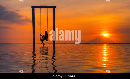 Silhouette di una donna seduta su un altalena in mare al tramonto, Indonesia Foto Stock