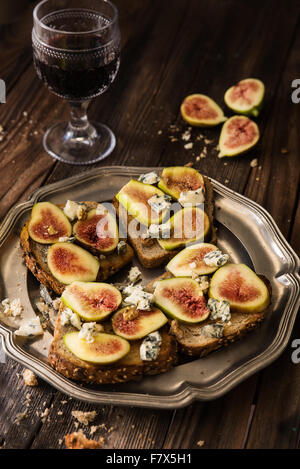 Figg, blu di formaggio e miele su pane tostato con un bicchiere di vino rosso Foto Stock