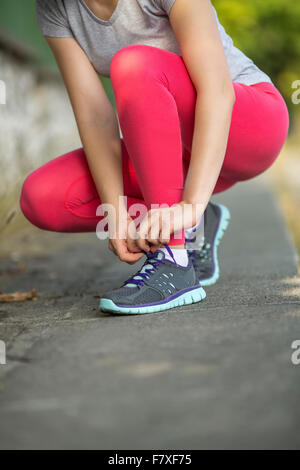 Closeup giovane ragazza sportiva legatura sui lacci delle scarpe sneakers all'esterno. Foto Stock