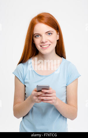 Ritratto di un sorridente redhead donna utilizza lo smartphone isolato su uno sfondo bianco Foto Stock