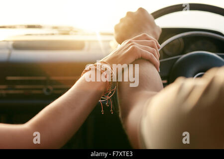 Immagine ravvicinata di amare giovane che viaggiano in auto e tenendo le mani. Focus sulle mani di un uomo e di una donna in un viaggio su strada. Foto Stock