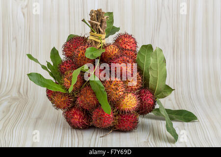 Rambutan fresco con foglie sullo sfondo di legno Foto Stock