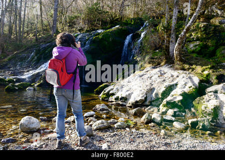Una donna fotografo fotografare una cascata, in autunno Foto Stock