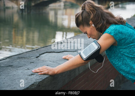 Giovane donna in abbigliamento sportivo e con lettore mp3 la cattura di respirare al Lungarno a Firenze, Italia Foto Stock