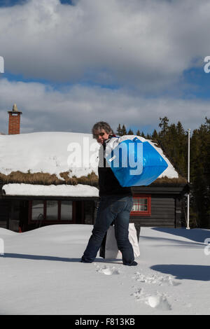 Uomo borse e zaini nella neve profonda di una tradizionale baita norvegese - Ritratto Foto Stock