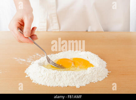 Lo chef sbattere le uova all'interno di farina su worksurface per pasta Foto Stock