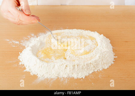 Lo chef sbattere le uova all'interno di farina su worksurface per pasta Foto Stock