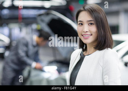 Giovane donna in officina di riparazione con la sua automobile Foto Stock