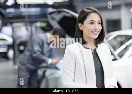 Giovane donna in officina di riparazione con la sua automobile Foto Stock