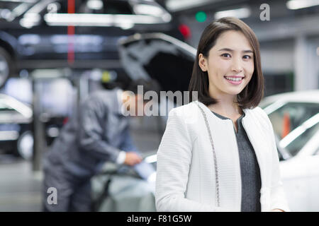 Giovane donna in officina di riparazione con la sua automobile Foto Stock