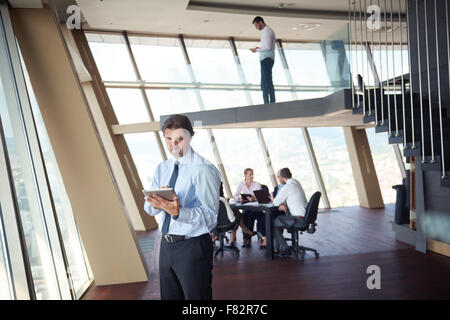 Business handosme uomo che lavora sul computer tavoletta al moderno luminoso ufficio in ambienti interni con il suo team nel gruppo a lavorare insieme nel retro Foto Stock