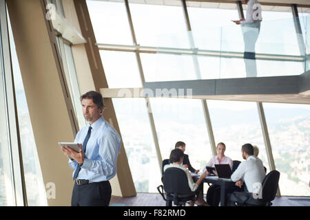 Business handosme uomo che lavora sul computer tavoletta al moderno luminoso ufficio in ambienti interni con il suo team nel gruppo a lavorare insieme nel retro Foto Stock