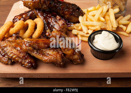 Ali di pollo e costolette con patate fritte sul tavolo di legno Foto Stock