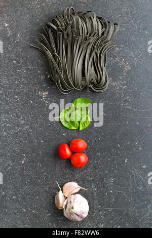 Tagliatelle, aglio, pomodori e basilico foglie sul vecchio tavolo da cucina Foto Stock
