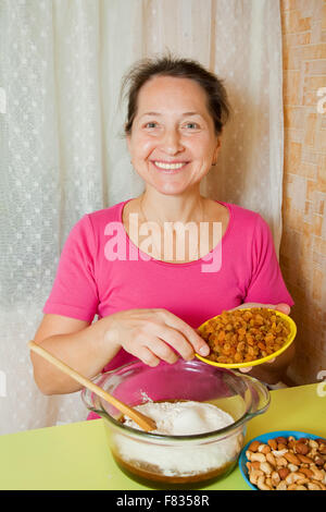 La donna aggiunge raisin in pasta. Una delle fasi del processo di cottura della torta di miele. Vedere serie Foto Stock