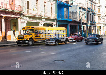 La dimensione del giallo scuolabus può essere visto qui contro alcune vecchie auto nel centro di Havana. Foto Stock