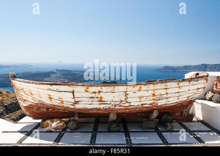 Santorini, Imerovigli. Il caldare visto dalla scogliera terrazza con il vecchio weathered vernice scrostata barca a remi con lo zenzero gatto dorme sotto. Foto Stock