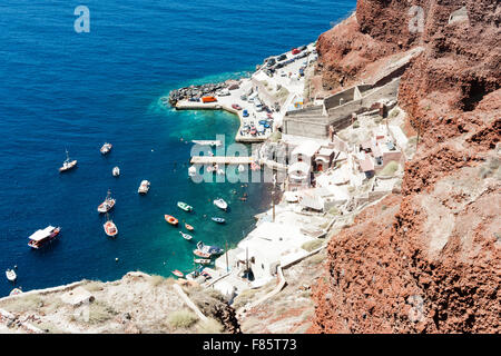 Santorini, Oia. Vista aerea. Ammoudi Beach, il Waterfront cubiform case, taverne e ristoranti con porto e barche da pesca in verde mare blu. Foto Stock