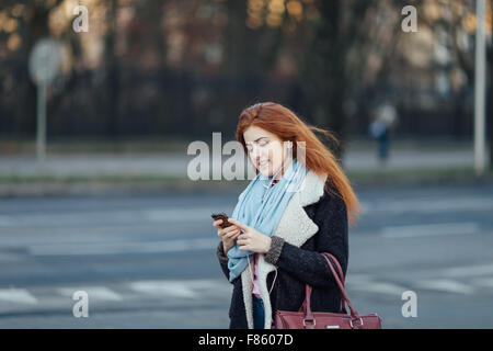 I Capelli rossi ragazza camminare per strada e ascoltare la musica sul suo telefono Foto Stock