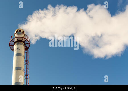 Singola alta ciminiera industriale emette lunghi pennacchi di fumo e di inquinamento in un chiaro e nitido cielo blu Foto Stock