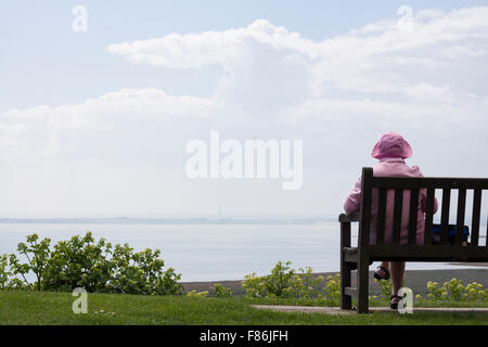 Pensionato inglese donna seduta sul banco di lavoro e gode di vista mare. Foto Stock