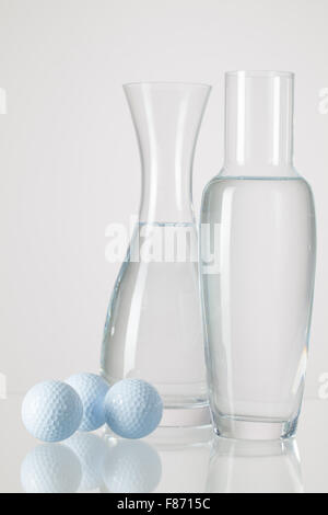 Due vasi con acqua pulita e palline da golf su un tavolo di vetro Foto Stock