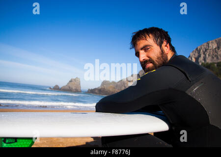 Surfer seduto sulla spiaggia con il suo bordo al mare Foto Stock