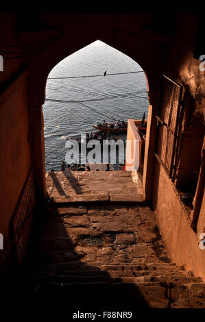 Vista da un edificio antico cancello alcuni pellegrini utilizzo di barche per attraversare il fiume sacro Gange per raggiungere la loro destinazione in Varanasi city. Foto Stock