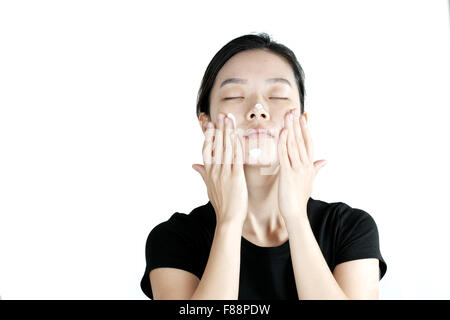 Carino ragazza asiatica di applicare la crema lozione sulla faccia, isolati su sfondo bianco Foto Stock