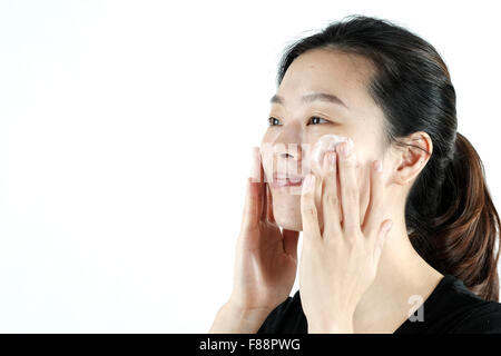 Carino ragazza asiatica di applicare la crema lozione sulla faccia, isolati su sfondo bianco Foto Stock