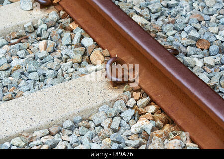 Primo piano della ferrovia arrugginito e calcestruzzo rinforzato marciapiede su un letto zavorrato Foto Stock