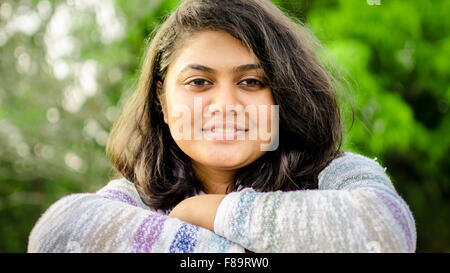 Close-up verticale di un equo chubby Indian ragazza adolescente mani piegate guardando la fotocamera sulla natura dello sfondo. Foto Stock